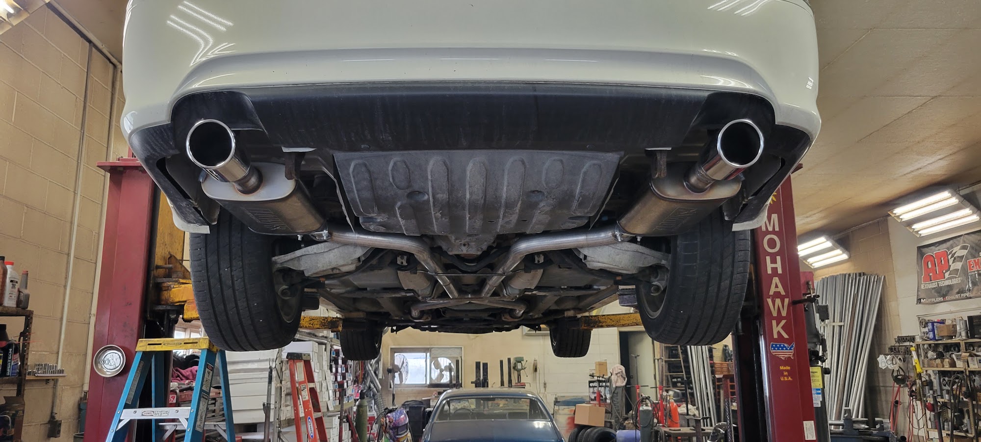 White car on a lift at Old Gold Auto Shop showing custom dual exhaust tips